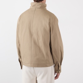 Model wearing Burberry saltmarsh beige cotton outerwear jacket, rear view, styled with white trousers.