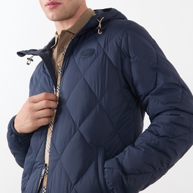 Model wearing Burberry navy quilted hooded jacket with diamond pattern, styled with a beige polo shirt. Checked lining detail visible.