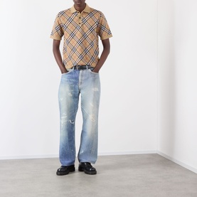 Model wearing Burberry Marlow Check Polo Shirt in Sand IP Check, styled with light wash distressed jeans and black loafers.