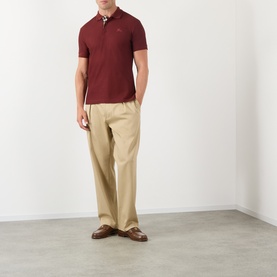 Model wearing Burberry red cotton polo shirt with check collar detail, styled with beige wide-leg trousers and brown loafers.
