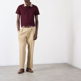 Model wearing Burberry Evan Check Polo Shirt in Vineyard Red with check collar, styled with beige trousers and brown leather shoes.