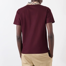 Model wearing Burberry Evan Check Polo Shirt in Vineyard Red, rear view, with check collar detail visible. Styled with beige trousers.