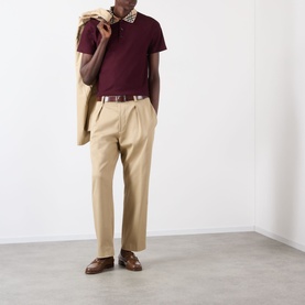 Model wearing Burberry Evan Check Polo Shirt in Vineyard Red with check collar, styled with beige trousers and blazer draped over shoulder.