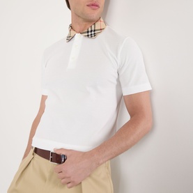 Model wearing Burberry white cotton polo shirt with signature check collar detail, styled with beige chinos and brown belt.