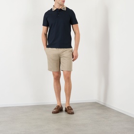 Model wearing Burberry Evan Burberry Check Polo Shirt in navy with check collar, styled with stone chino shorts and brown loafers.