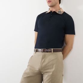 Model wearing Burberry Evan Burberry Check Polo Shirt in navy with check collar detail, styled with beige chinos and brown leather belt.