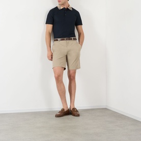 Model wearing Burberry Evan Burberry Check Polo Shirt in navy, styled with beige chino shorts, brown belt, and tan loafers.