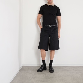 Model wearing Burberry black cotton polo shirt with bow tie collar detail, styled with black shorts, belt and chunky leather boots.