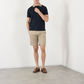 Model wearing Burberry Charlton Embroidered Logo Chino Shorts in saltmarsh beige, styled with a navy polo shirt and brown loafers.
