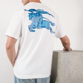 Model wearing Burberry white cotton T-shirt, back view showing large blue Equestrian Knight graphic print, paired with light blue jeans.