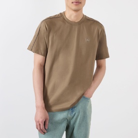 Model wearing Burberry Seth Check Piping T-Shirt in Finch Brown with check shoulder piping and embroidered logo, styled with light blue jeans.