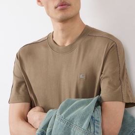 Model wearing Burberry Seth Check Piping T-Shirt in Finch Brown with embroidered logo, check piping at shoulders, styled with denim jacket.