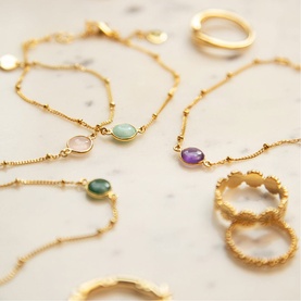 Daisy Jewellery Healing Stone Bobble Bracelet in 18ct gold plate with coloured gemstone pendants, styled with rings on marble surface.
