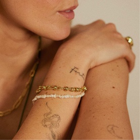 Model with Daisy Jewellery Polly Knot Chain Bracelet in 18ct gold plate; chunky knot links, styled with delicate beaded bracelet and gold chain