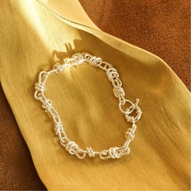 Daisy Jewellery Polly Knot Chain Bracelet in sterling silver with bold knot links and toggle clasp, styled on golden fabric.