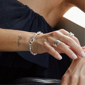 Model with Daisy Jewellery Polly Knot Chain Bracelet in sterling silver, bold knot links on wrist, styled with silver rings, navy top visible.