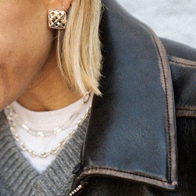 Model with Daisy Jewellery Polly Mini Woven Square Studs in sterling silver, styled with layered chain necklaces and a dark leather jacket