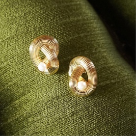 Daisy Jewellery Polly Ties The Knot Pearl Studs in 18ct gold plate, sculptural knot design with pearl detail, on green fabric background