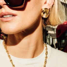 Model with Daisy Jewellery Polly Ties The Knot Pearl Studs in 18ct gold plate, sculptural knot design; styled with gold chain necklace and sunglasses