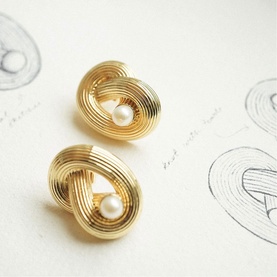 Daisy Jewellery Polly Ties The Knot Pearl Studs in 18ct gold plate, sculptural knot design with central pearl, shown on sketch background