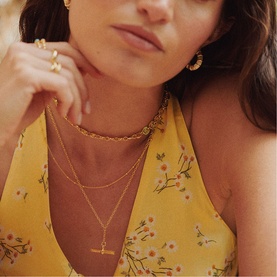 Model with Daisy Jewellery Est&eacute;e Lalonde T-Bar Necklace in 18ct gold plate, layered with gold chain necklaces and hoop earrings