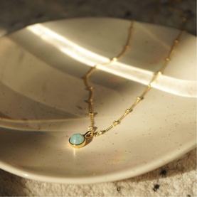 Daisy Jewellery Healing Stone Necklace in 18ct gold plate with round amazonite stone pendant on adjustable bobble chain, resting on ceramic dish