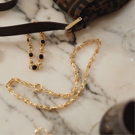 Daisy Jewellery Polly Knot Chain Necklace in 18ct gold plate with bold knot links and classic clasp, styled on marble surface