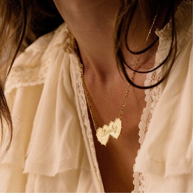 Model with Daisy Jewellery Shrimps Double Heart Lucky Necklace in 18ct gold plate, layered on a dark cord chain, styled with ivory lace top.