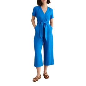 Model wearing Hobbs sapphire blue short-sleeve wrap-style jumpsuit with tie waist and cropped wide-leg trousers, styled with tan sandals