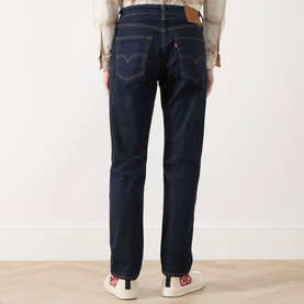 Model wearing Levi's dark blue jeans, rear view, straight leg fit with signature back pocket tab, styled with a beige shirt and white trainers.
