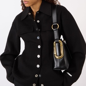 Model carrying Marc Jacobs Scene Logo Shoulder Bag in black leather with gold-toned hardware, styled with a black button-through shirt