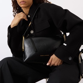 Model carrying Marc Jacobs Scene Logo Shoulder Bag in black leather with gold-toned hardware and top-zip fastening, styled with black tailored outfit