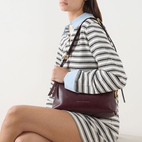 Model carrying Marc Jacobs Scene Logo Shoulder Bag in dark port leather with gold-toned hardware, styled with striped blazer and shorts