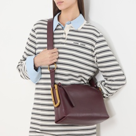 Model carrying Marc Jacobs Scene Logo Shoulder Bag in dark port leather, gold-toned hardware, worn crossbody over striped rugby shirt.