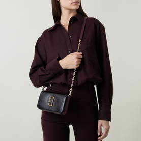 Model carrying Marc Jacobs The Snapshot On Chain Wallet in black multi, gold-toned curb chain strap and hardware, styled with dark burgundy shirt and