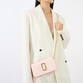 Model carrying Marc Jacobs The Snapshot On Chain Wallet in powder pink multi, gold-toned hardware and curb chain strap, styled with cream blazer.