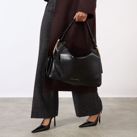 Model carrying Marc Jacobs The Scene Large Shoulder Bag in black smooth leather with gold-tone hardware, styled with wide-leg trousers and heels