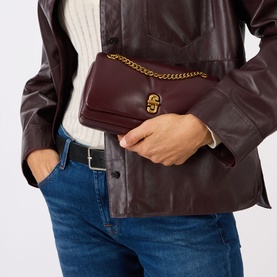 Model carrying Marc Jacobs The Dual Chain Mini Bag in Dark Port, gold-tone chain strap and double J turn-lock closure, styled with leather jacket and