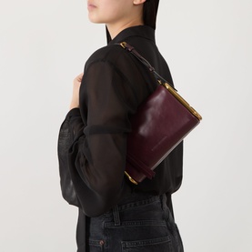 Model carrying Marc Jacobs Scene Small Shoulder Bag in dark port leather with gold-toned hardware, styled with black blouse and jeans