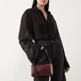 Model carrying Marc Jacobs Scene Small Shoulder Bag in dark port leather with gold-toned hardware, worn crossbody, styled with black shirt and jeans