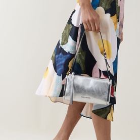 Model carrying Marc Jacobs Scene Small Shoulder Bag in silver metallic leather with zip-top and silver-tone hardware, styled with a floral midi skirt