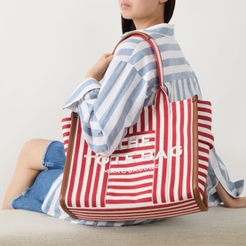 Model carrying Marc Jacobs The Stripe Canvas Large Tote Bag in True Red Multi, gold-tone hardware, leather trim, styled with a striped shirt