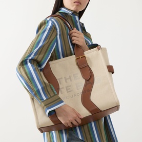 Model carrying Marc Jacobs The Wavy Canvas Large Tote Bag in beige/argan oil with tan leather trim, gold-tone hardware, and carry handles