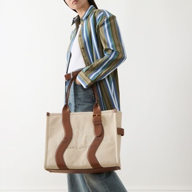 Model carrying Marc Jacobs The Wavy Canvas Large Tote Bag in beige, brown leather trim, gold-tone hardware, styled with striped shirt and jeans