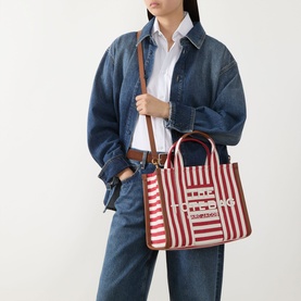 Model carrying Marc Jacobs The Striped Canvas Medium Tote Bag in True Red Multi with brown leather crossbody strap, styled with denim jacket and jeans