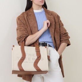 Model carrying Marc Jacobs The Wavy Canvas Medium Tote Bag in beige/argan oil with brown leather wavy trim and top handles, styled with suede blazer