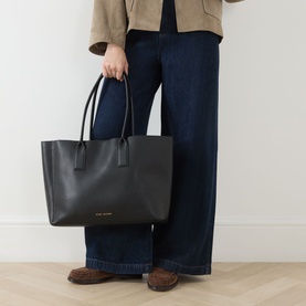 Model carrying Marc Jacobs The Pop J Marc Work Tote in black grained leather with gold-tone hardware and twin carry handles, styled with wide-leg