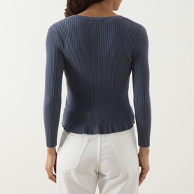 Model wearing Paige Pacific Blue ribbed cardigan, back view, with fluted hem and long sleeves, styled with white trousers.