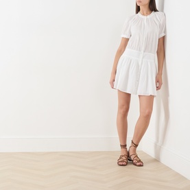 Model wearing Paige white cotton mini dress with short sleeves and tiered skirt, styled with tan lace-up flat sandals