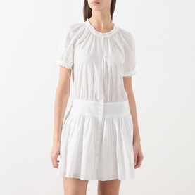 Model wearing Paige white cotton mini dress with ruched neckline, puff sleeves and pleated skirt.